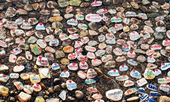 Vibrant painted stones with names on a rocky Italian beach, creating a lively artistic scene.