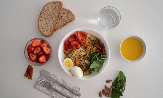 A balanced meal featuring a variety of healthy ingredients including noodles, eggs, almonds, strawberries, and fresh vegetables.
